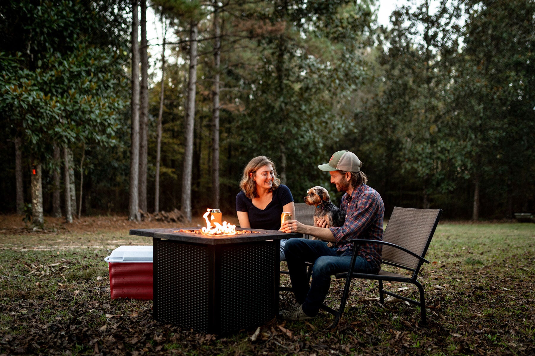 A couple and their dog around a fire pit in a backyard at dusk